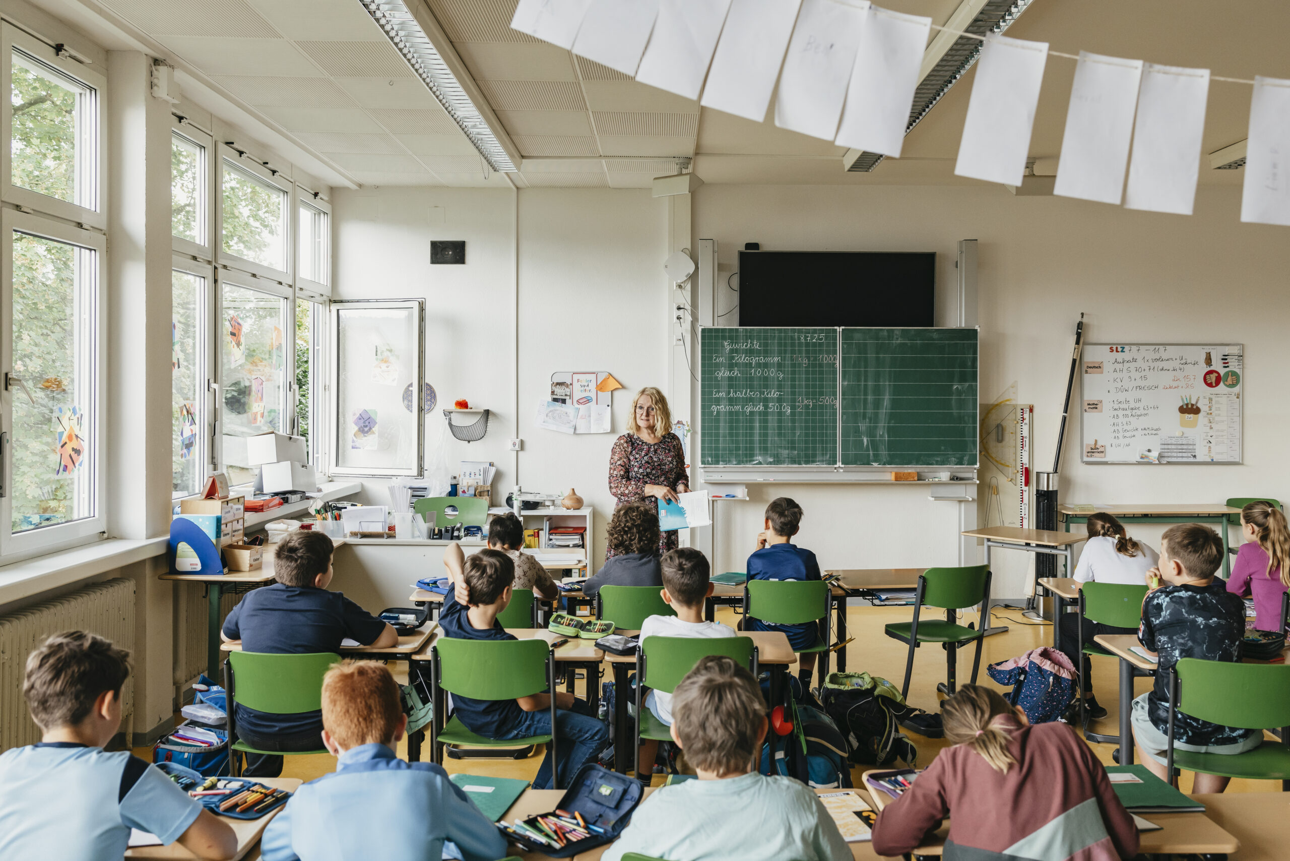 Eine Lehrerin in einer Grundschule steht vor der Klasse und zeigt etwas in einem Buch