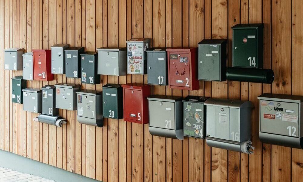 Viele unterschiedliche Briefkästen in zwei Reihen an einer Holzwand.